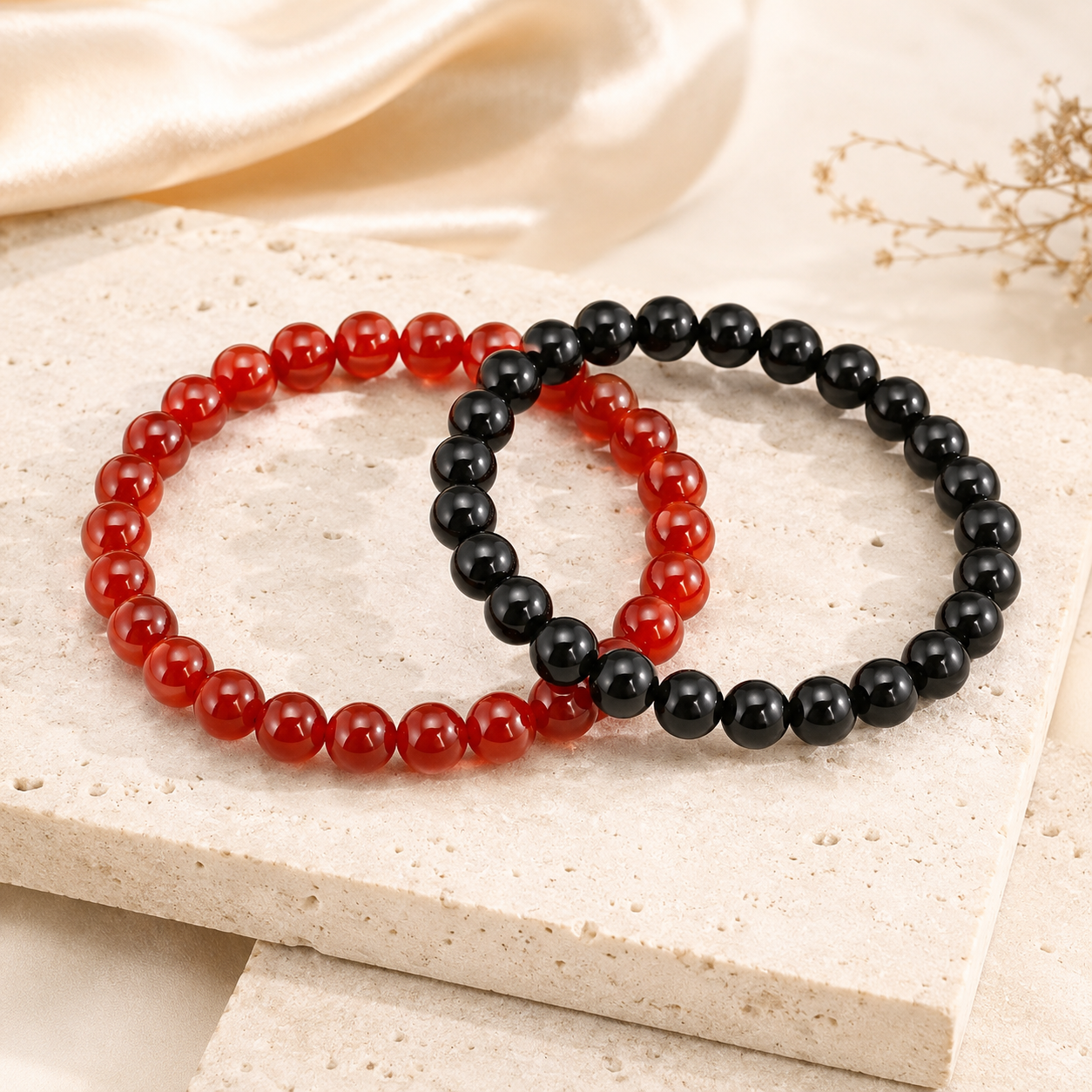 Black obsidian and red carnelian couple bracelets on warm ivory stone